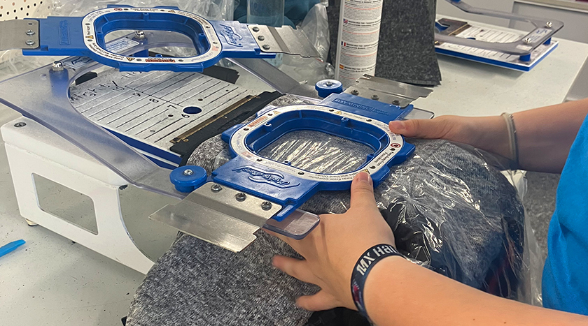 Antholzer Mitarbeiterin in der In-House Stickerei in Vilsbiburg Bayern, beim Einspannen von Arbeitskleidung in den Stickrahmen als Vorbereitung für den Textilstick mit dem Firmenlogo.